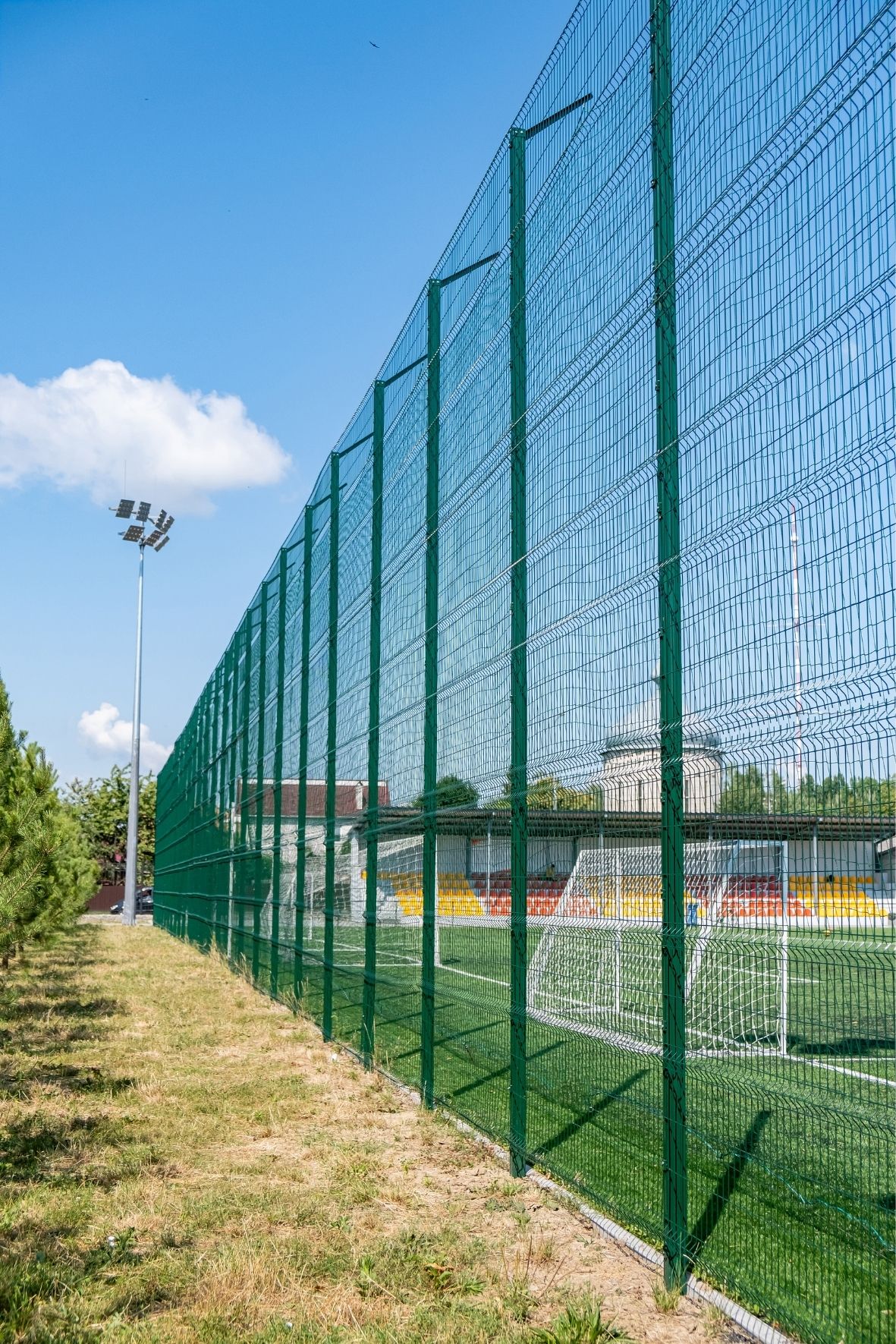 Clôture métallique haute entourant un terrain sportif extérieur avec structures visibles en arrière-plan  dans le Bas-Saint-Laurent